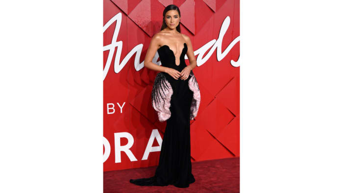 Olivia Culpo poses on a red carpet in a plunging black figure-hugging gown.